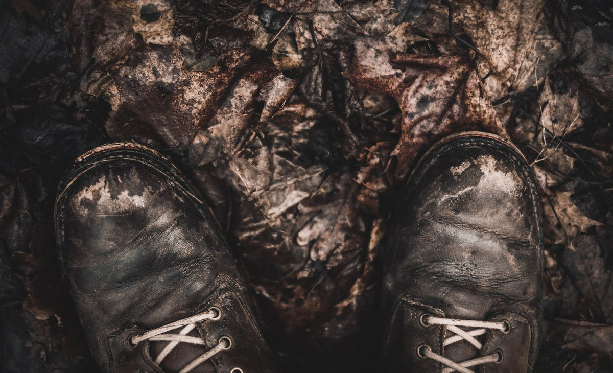 Close-up of worn, muddy hiking boots on a forest trail covered in fallen autumn leaves