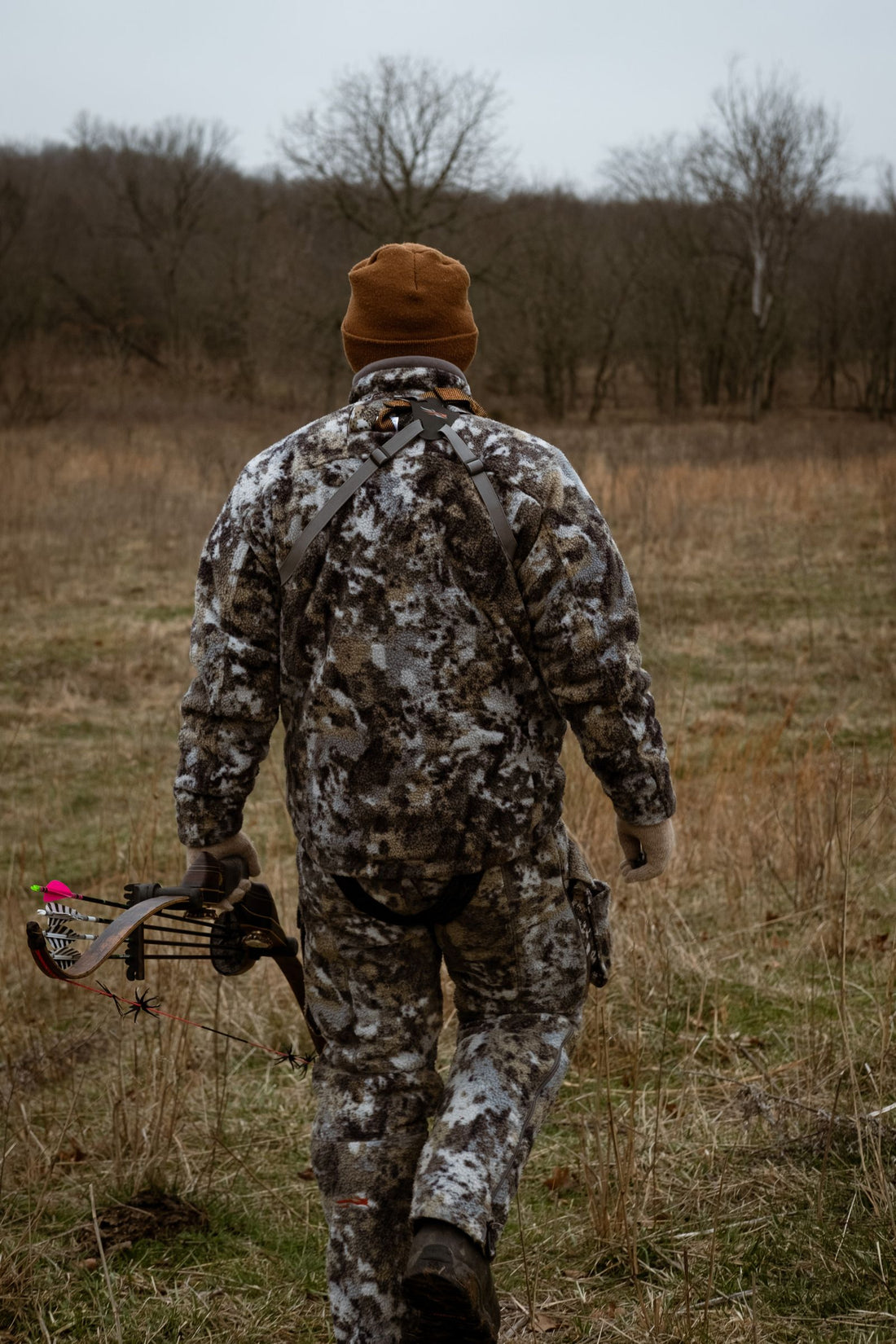 Bowhunter in camouflage carrying a bow through an autumn field during archery season