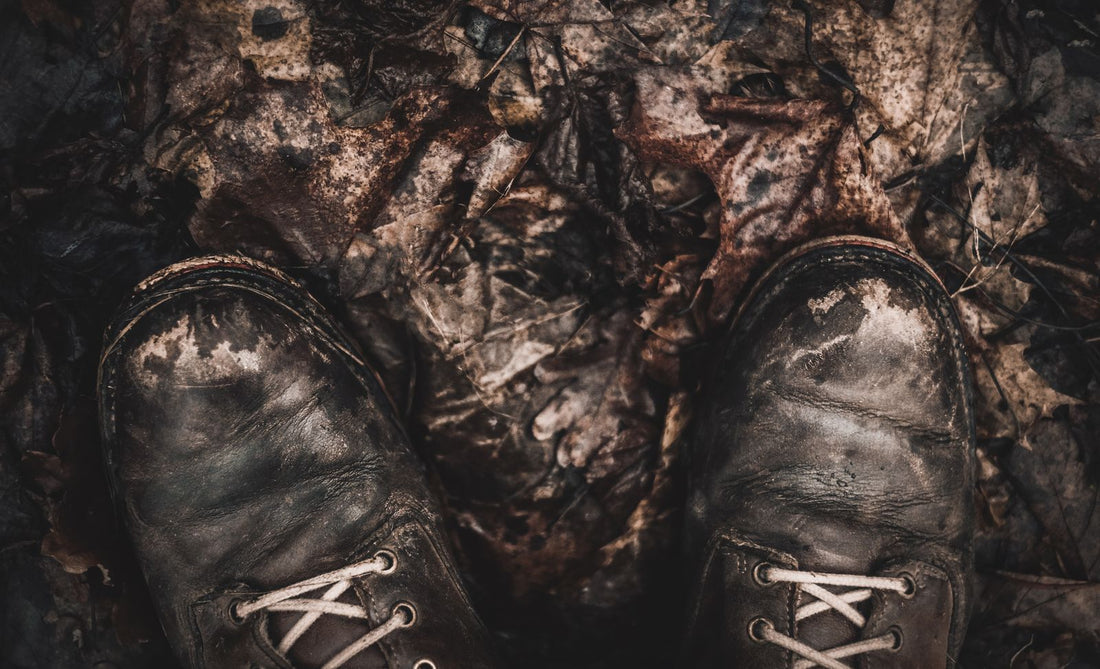 Close-up of worn, muddy hiking boots on a forest trail covered in fallen autumn leaves