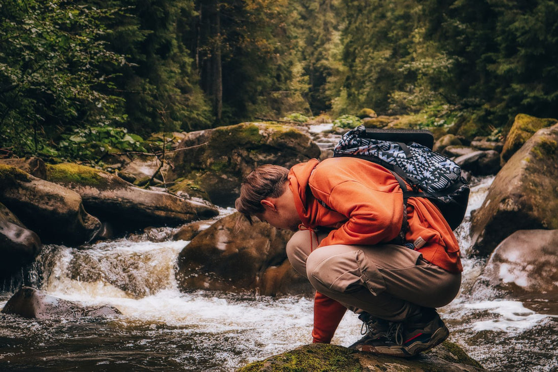 Backpacker crouching beside a forest stream surrounded by orange and gold fall foliage on an autumn hiking trip