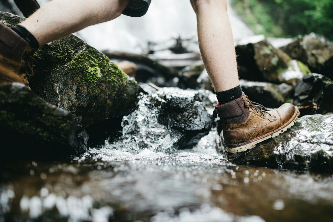 Hiker in leather boots stepping across mossy rocks on a creek crossing