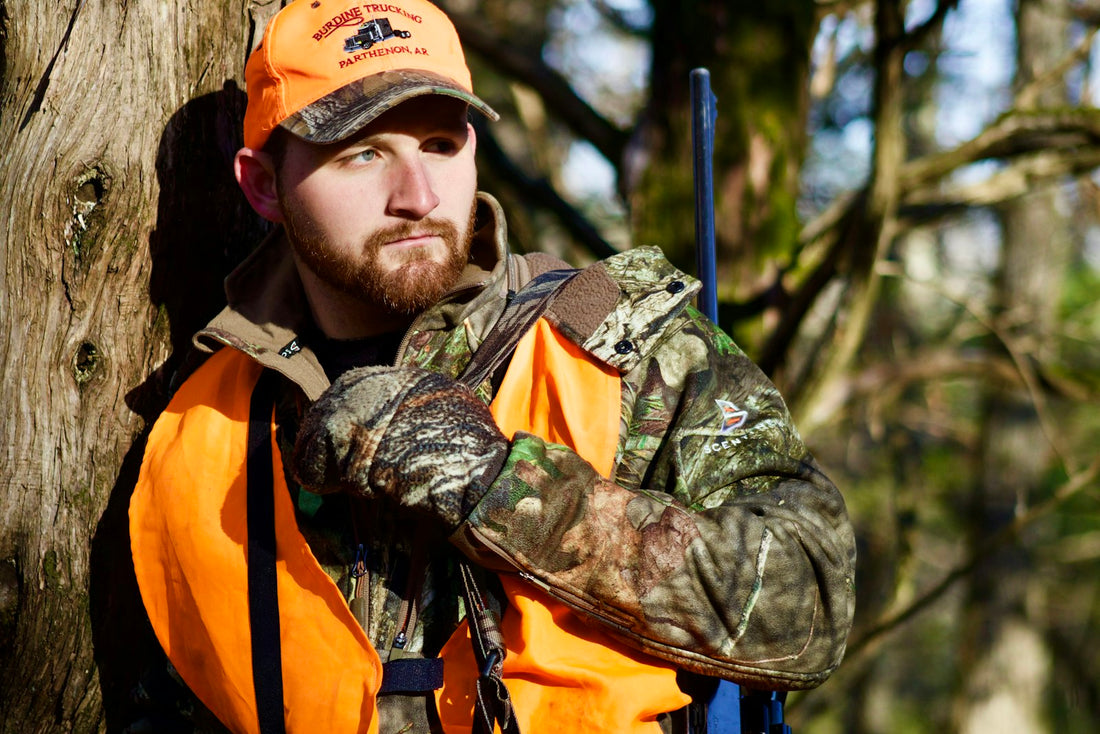 Deer hunter in a camouflage jacket and orange-and-black pack walking through the woods